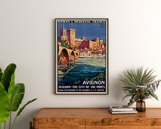 Vintage turistplakat – Avignon, romansk og middelalderlig Frankrig, indrammet over en kommode i træ, flankeret af planter.