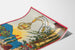 Vintage vinplakat – Au bon vin d’Alsace – Hansi, vist på et buet ark i perspektiv.