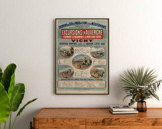 Vintage plakat Auvergne, udflugter PLM, indrammet over en kommode i træ mellem planter.