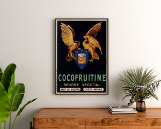 Vintageplakat Cocofruitine, vegetabilsk smør, indrammet over en trækommode, mellem planter.